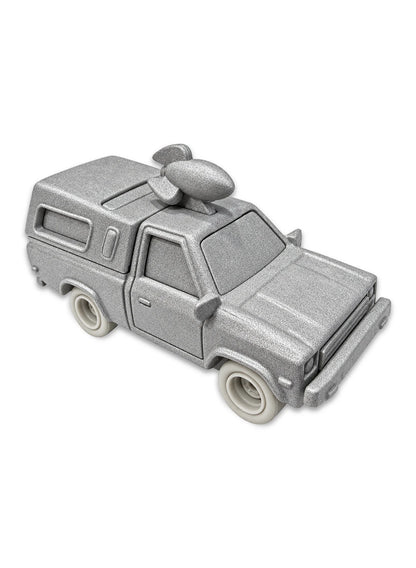 Close-up view of the stone-textured matte grey Hot Wheels The Good Dinosaur Pizza Planet Truck showing a sculpted fossilized rocket ship roof topper, rugged prehistoric truck panels, and matching grey stone Real Riders wheels.